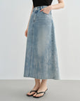 Person wearing a long denim skirt on a plain background