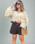 Woman wearing a white blouse with ruffled sleeves, dark shorts, and sunglasses outdoors.