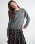 Woman wearing a gray sweater and plaid skirt on a white background