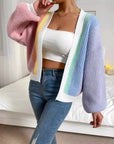 Person wearing a colorful cardigan over a white top and blue jeans in a bedroom setting.