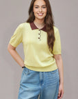 Woman wearing a yellow polo shirt with a brown collar and blue jeans on a gray background
