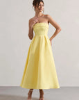Woman wearing a yellow strapless dress against a plain background