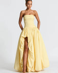 Woman wearing a yellow strapless gown with a high slit on a white background