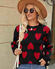Woman wearing a black sweater with red heart patterns, sunglasses, and a hat.
