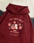 Maroon hoodie with strawberry design and text on a textured surface