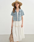 Woman wearing a denim vest over a white dress with a straw hat on a plain background
