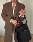 Person wearing a brown coat holding a black handbag indoors.