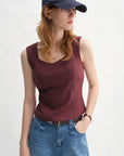 Woman wearing a maroon sleeveless top and blue jeans with a navy cap on a white background