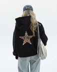 Person wearing a black hoodie with a leopard print star on the back, walking on a street.