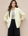Woman wearing a light yellow blazer over a striped shirt and black skirt on a beige background