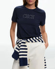 Person wearing a navy blue t-shirt with 'CHCH' text, white pants, and a navy and white striped top.