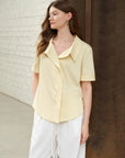 Woman wearing a light yellow blouse and white pants against a neutral background