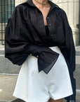 Person wearing a black oversized shirt with a bow tie and white shorts outdoors.