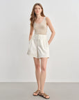 Woman wearing a beige sleeveless top and white shorts on a plain background
