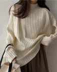 Person wearing a white ribbed sweater with a neutral background