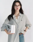 Woman wearing a striped shirt and jeans, holding a book against a white background