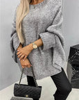 Person wearing a gray oversized sweater and black pants, holding a black quilted handbag.