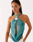 Woman wearing a teal halter top with a large white pendant on a white background