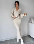 Woman in a beige ribbed sweater and pants holding a coffee cup indoors.
