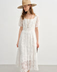 Woman wearing a white lace dress and straw hat on a plain background