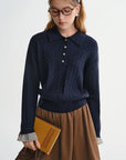 Person wearing a navy blue cable knit sweater and brown skirt, holding a book.